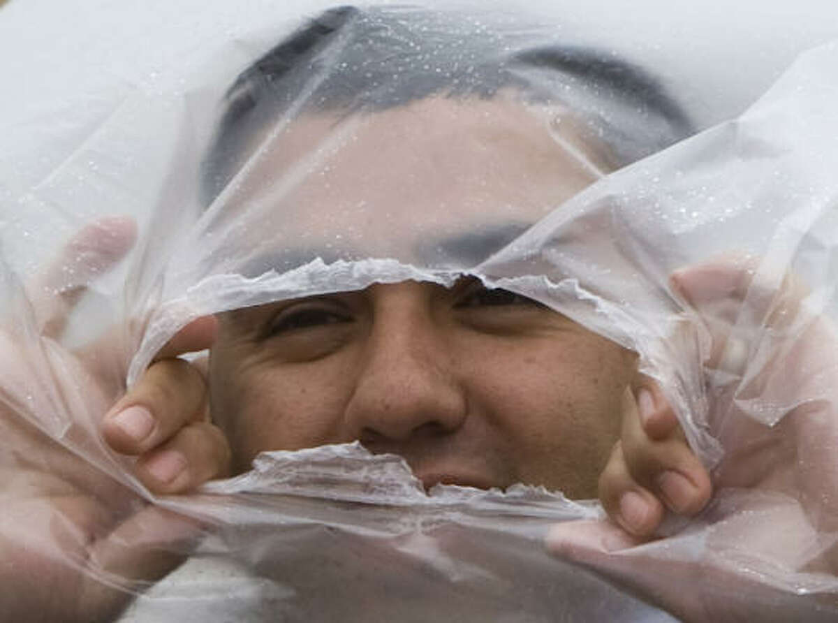 Augusin Esquivel peers through a hole in a plastic bag as he tries to stay dry in the wind and rain on the carnival midway at the Houston Livestock Show and Rodeo.