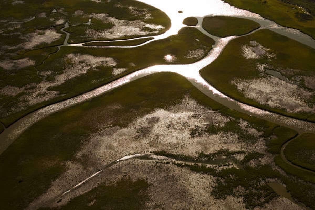 Water glistens ﻿as the sun sets on marshy Bolivar Peninsula wetlands ﻿near Port Bolivar. Experts estimate that every 2.7 miles of wetlands produce a protective barrier that reduces a storm's tidal surge by a foot. ﻿