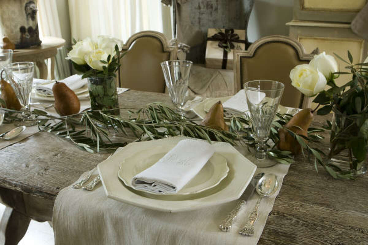 For the Museum District home of Dr. Devinder and Gina Bhatia, she and Megan Talley layered the painted French trestle dining table with olive branches, brown pears and white roses. Vintage linens, glassware and flatware, along with antique French dinnerwa