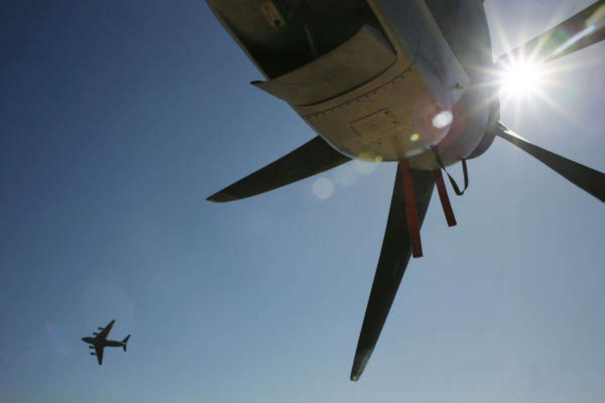 A C-17A flies past a parked C-130 at the airshow.