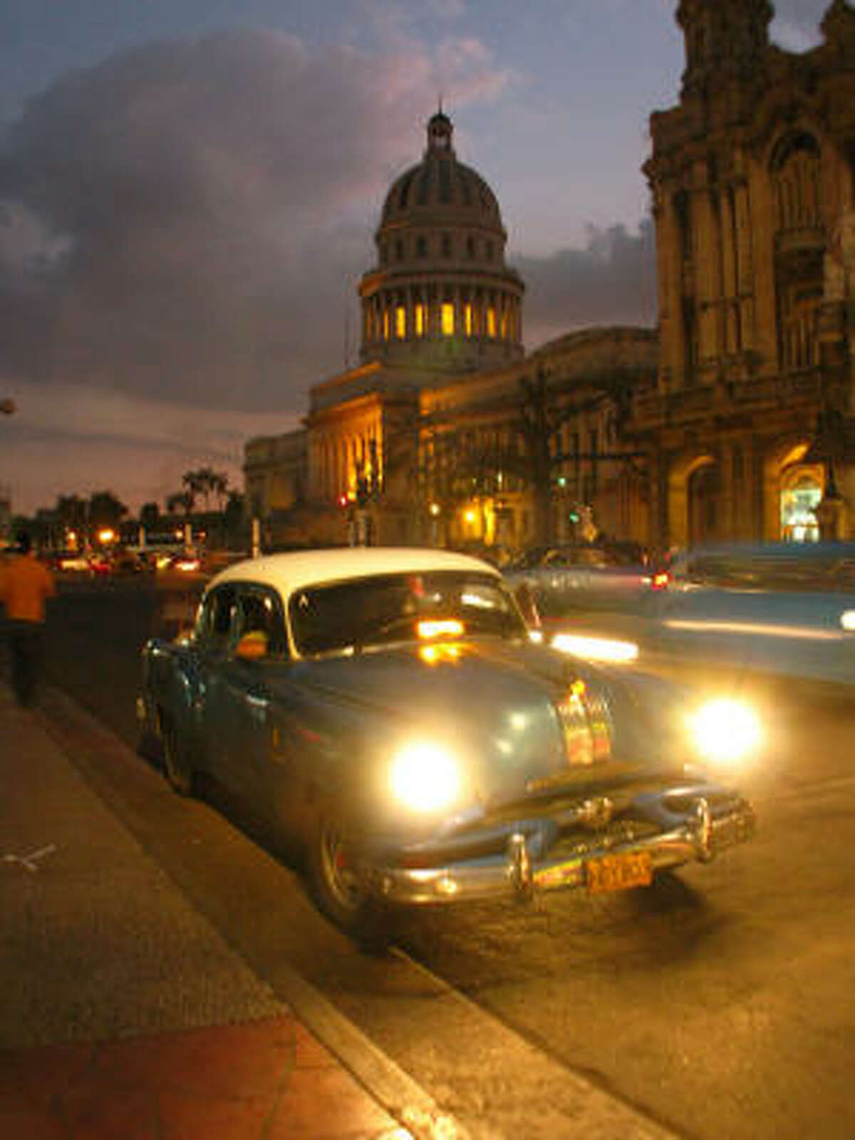 Hitchhikers jump into a classic 1950s car with the former National Capitol building in the background in Havana, Cuba.