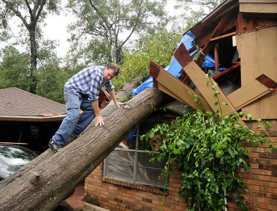 Sam Wilkinson climbs the tree that crashed into his mother's home. Wilkinson was covering the hole with plastic until the home can be fixed. Photo: David Hopper, For The Chronicle