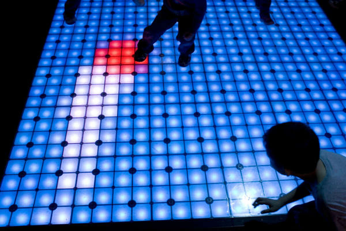 Children play an electronic game of dodge ball on a lit museum floor.