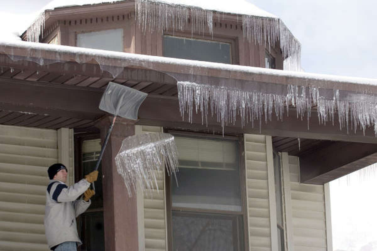 Brian VanSickle knocks icicles off his home in Evansville, Ind., Wednesday. The heaviest snowfall in 13 years buried central Indiana under a foot of snow Wednesday, shuttering schools and stores after ice brought down power lines.