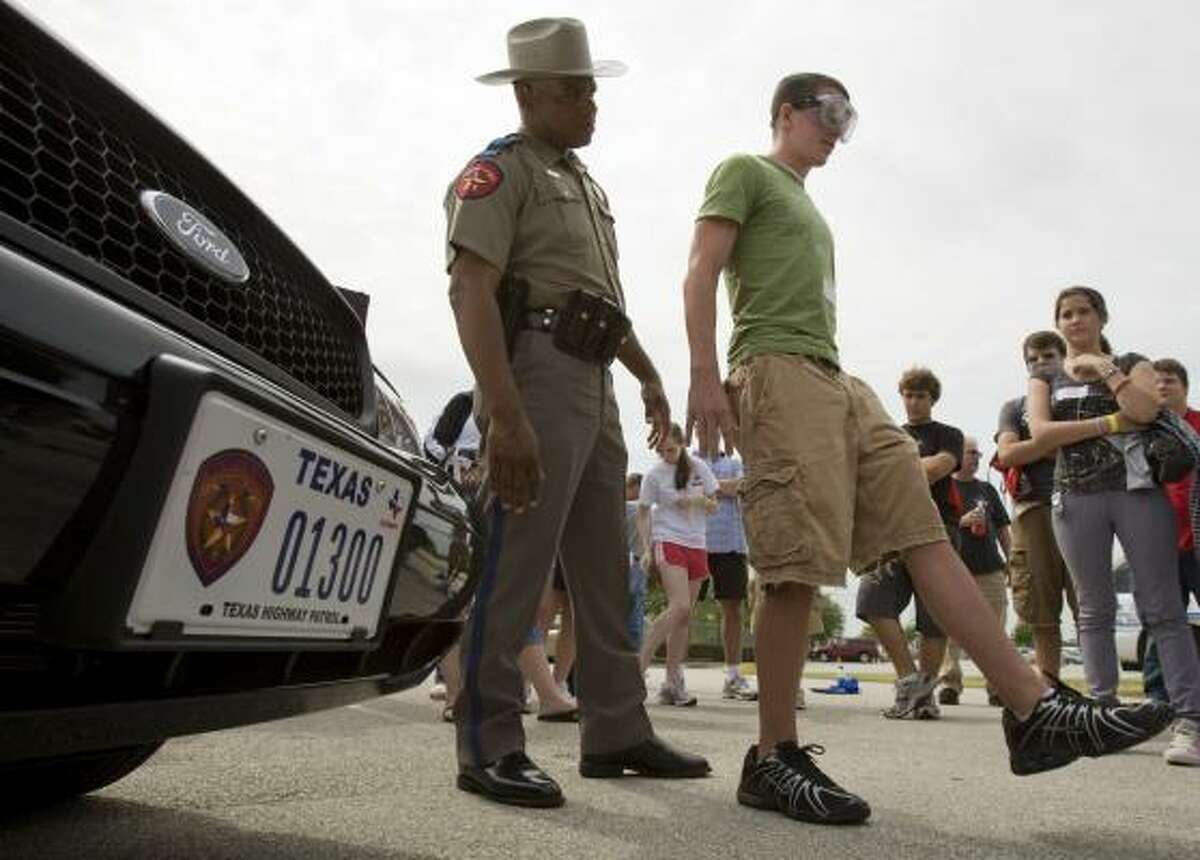 State Trooper John Sampa, left, keeps an eye on Warren Rooney, 16, as he attempts a field sobriety test while wearing "fatal vision goggles" at the Driver's Edge course at Reliant Park on Sunday. The goggles simulate the effects of being intoxicated.