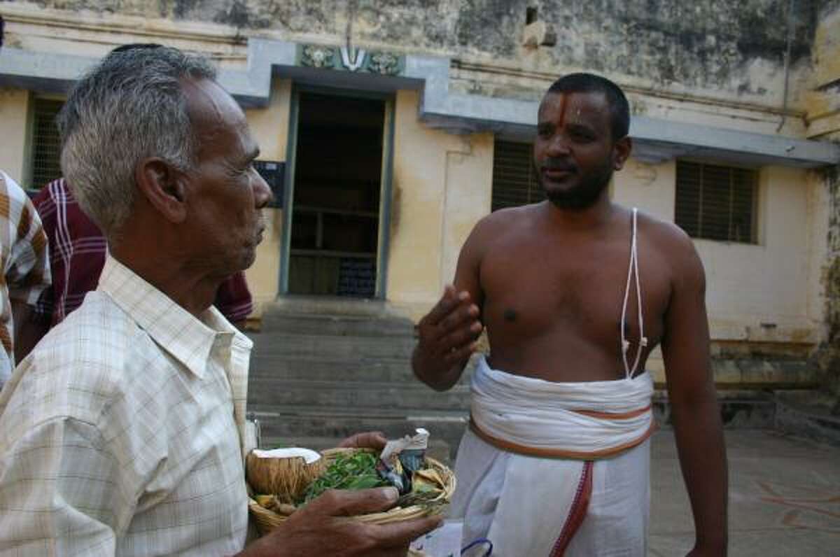 T.K. Jayaraaman, left, gives Balaji, a Hindu priest, a basket of offerings that Balaji will present to the god Vishnu on behalf of a woman in London who purchased the service, called a puja, on the Internet.