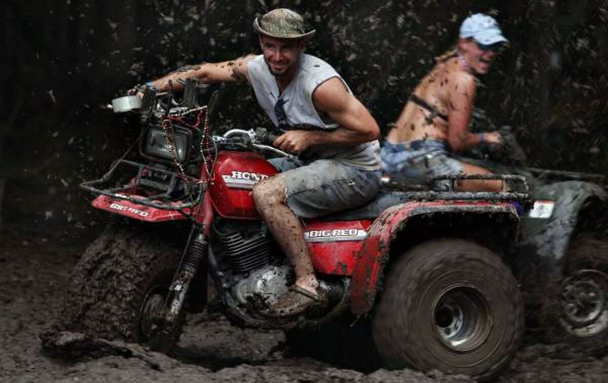 Larry Robichaux and Tonya Caldwell, of Baton Rouge, La., get dirty on all-terrain vehicles during the Texas Redneck Games at the Pool Ranch in Athens on Saturday.