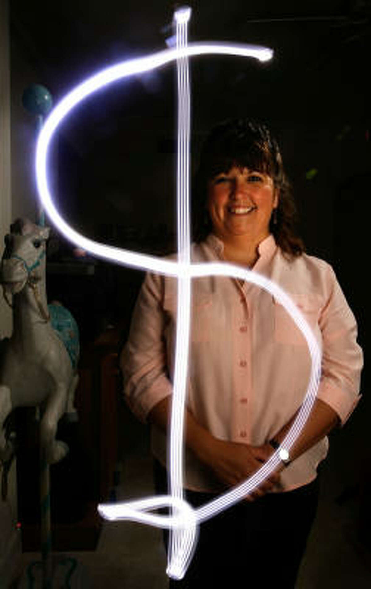Natasha Kelly uses a light to illustrate the money she saved on her utility bill by choosing a month-to-month plan. The photo is a single shot using a time exposure of Kelly tracing a dollar sign, followed by a flash to capture her image.