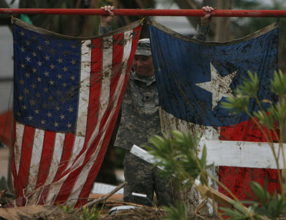 Tattered | Spc. Scott Hayes with the Texas Army National Guard holds up a muddied set of flags found in the destruction as guardsmen conduct search and rescue operations. | Sept. 14 | Galveston Photo: Sharon Steinmann, Houston Chronicle
