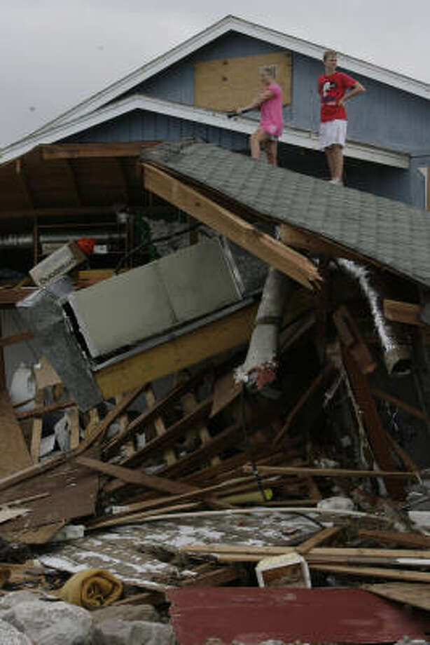 Up close | Kara Bridwell, 26, left, and her brother, Paul Bisso, 17, climb atop the roof of their neighbor's house, which washed into the front of their family's beach house. | Sept. 14 | Surfside Beach Photo: Julio Cortez, Houston Chronicle