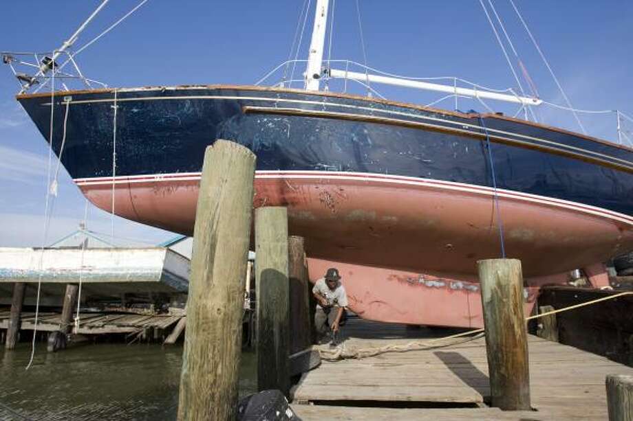Docked | Anh Ngo walks under a sailboat that washed up on the dock at a shrimp boat marina. | Sept. 15 | Galveston Photo: Brett Coomer, Houston Chronicle