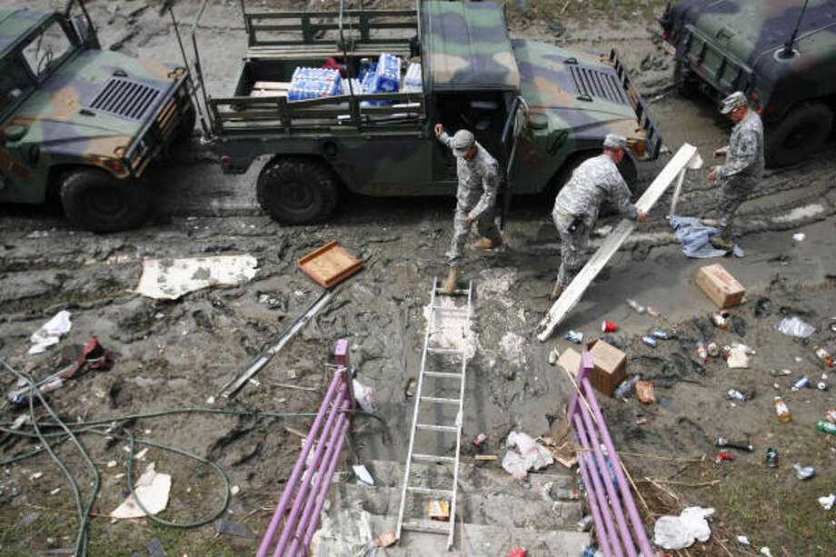 Holdouts | Texas Army National Guardsmen use a ladder and old boards to traverse the mud surrounding the Crystal Palace Resort. The troops delivered MREs and water to the five people who reÂfused to leave the hotel. | Sept. 17 | Crystal Beach Photo: Sharon Steinmann, Houston Chronicle