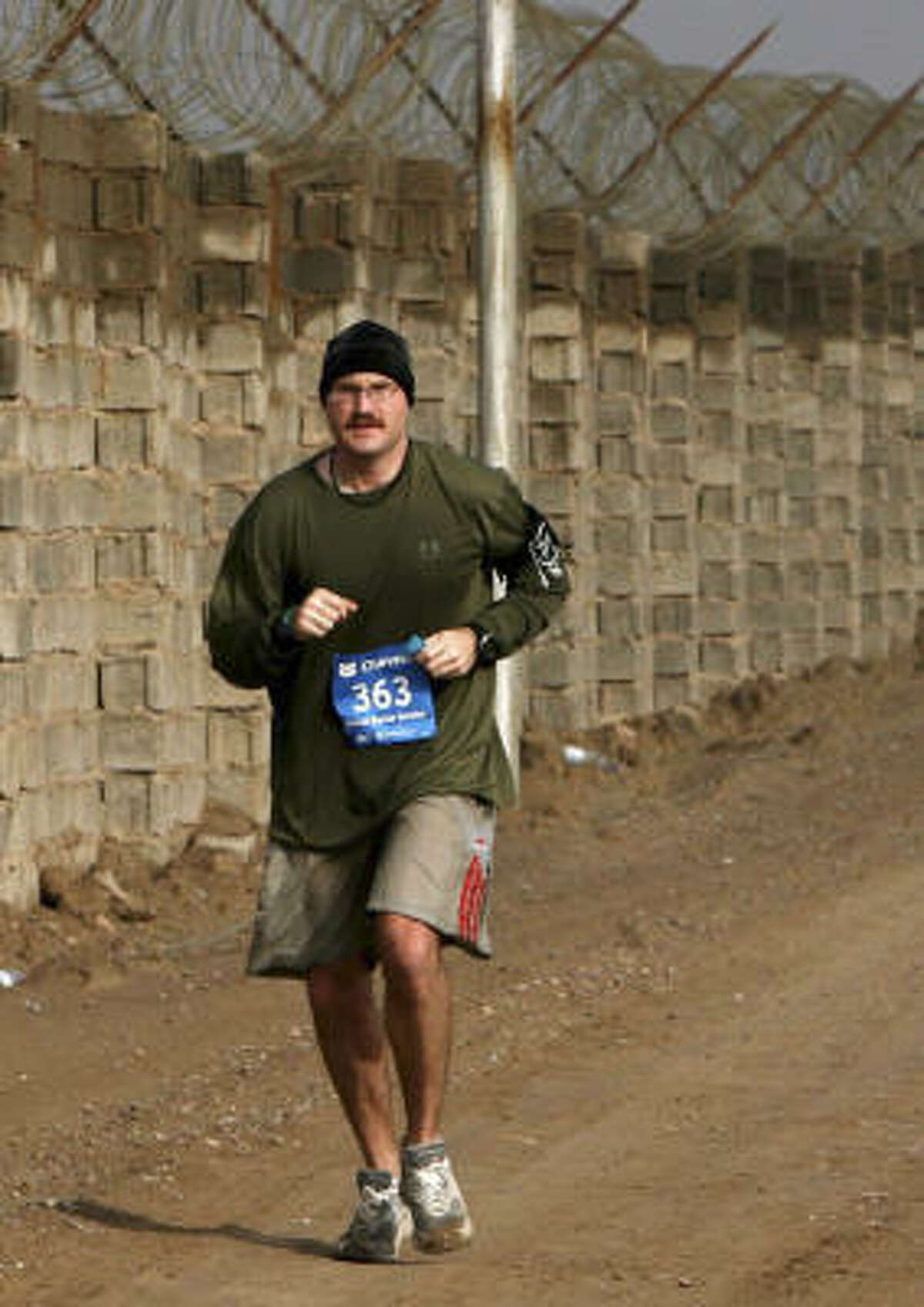 A Marine runs along a fence line during the Satellite Chevron Houston Marathon run in Camp Fallujah, Iraq. Since many soldiers couldn't come to the race, a version of the race came to them.
