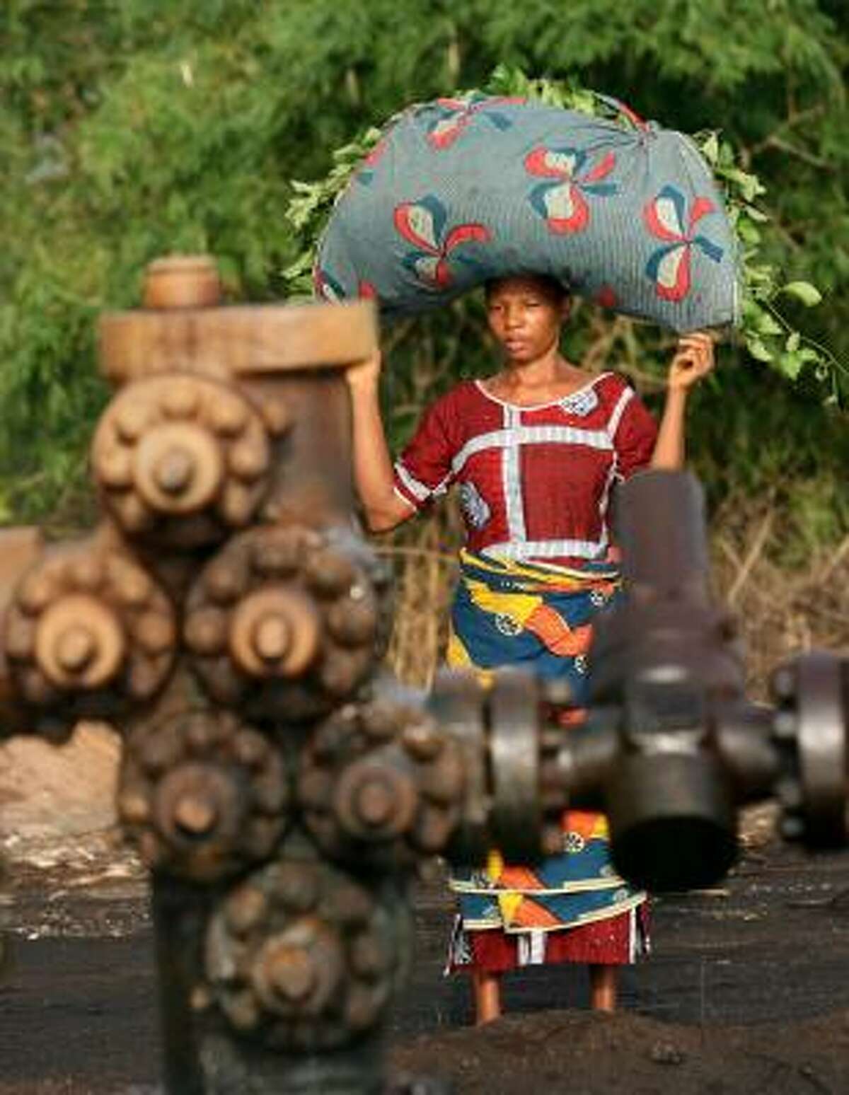 A woman returning from the fields passes a leaking oil well in Kegbara Dere, Nigeria. The country is looking to reform its agreements with international oil companies.