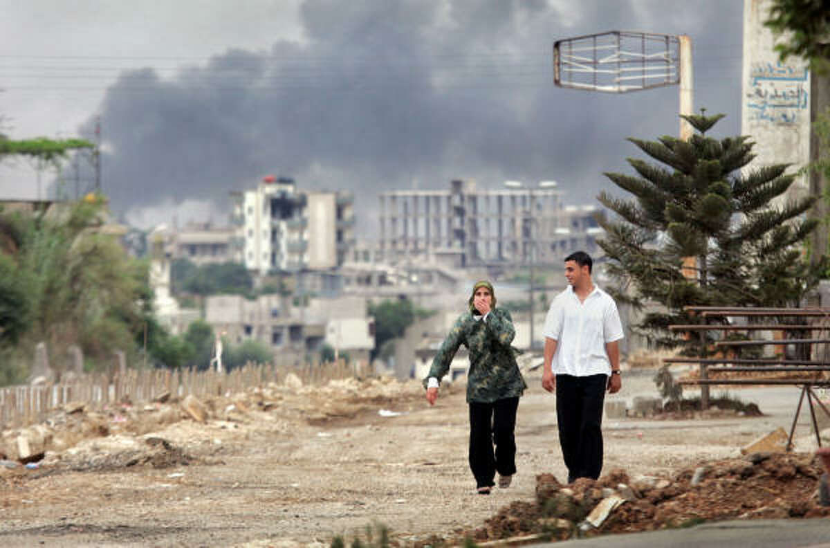 A woman covers her mouth with her hand as she walks with a man up the main road away from the besieged Nahr el-Bared refugee camp, as black smoke from explosions billowing into the sky.