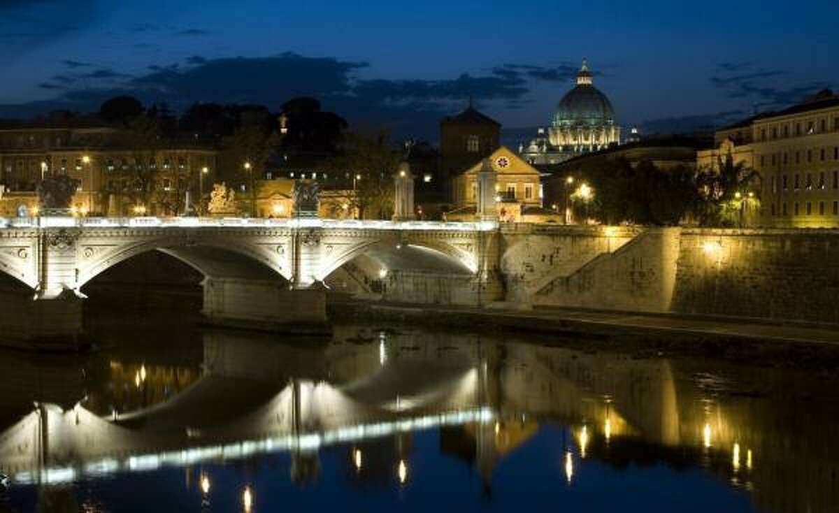 St. Peter's Basilica is illuminated as evening falls in Rome. Taverna Giulia restaurant is near the River Tiber just across the bridge.