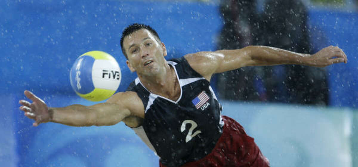 Sean Rosenthal, of the United States, dives under pouring rain for a ball during his men's Pool F preliminary beach volleyball match against The Netherlands.