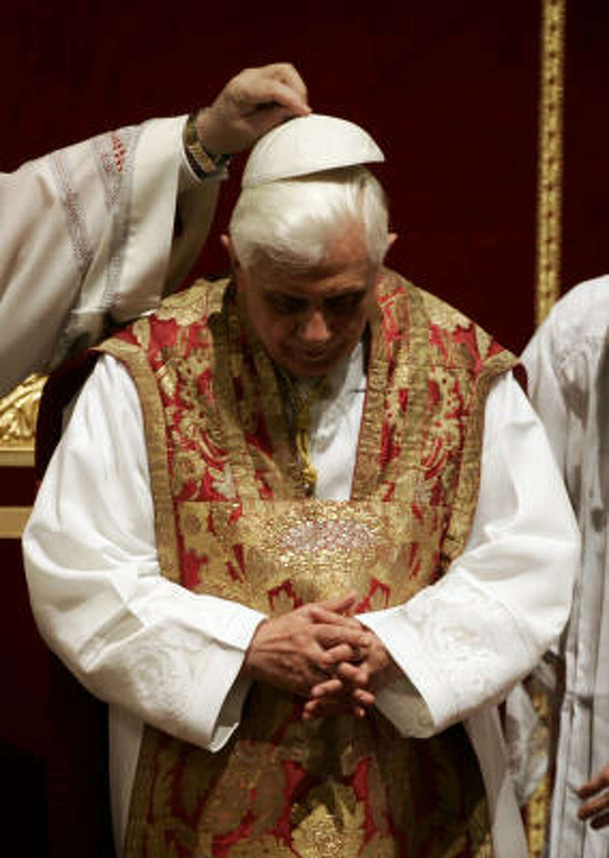 Pope Benedict XVI, wearing a fiddleback chasuble, has his cap placed back on his head after praying during a Mass for the unveiling and adoration of the Cross in St. Peter's Basilica in March.