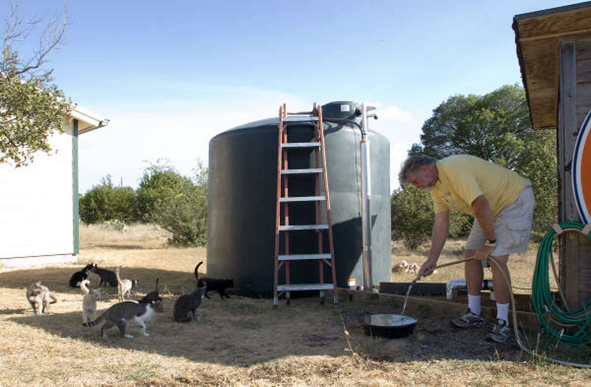 Wayland Clark gives water to his many cats in Dripping Springs. The drought has run his well dry, forcing him to have water delivered to him.