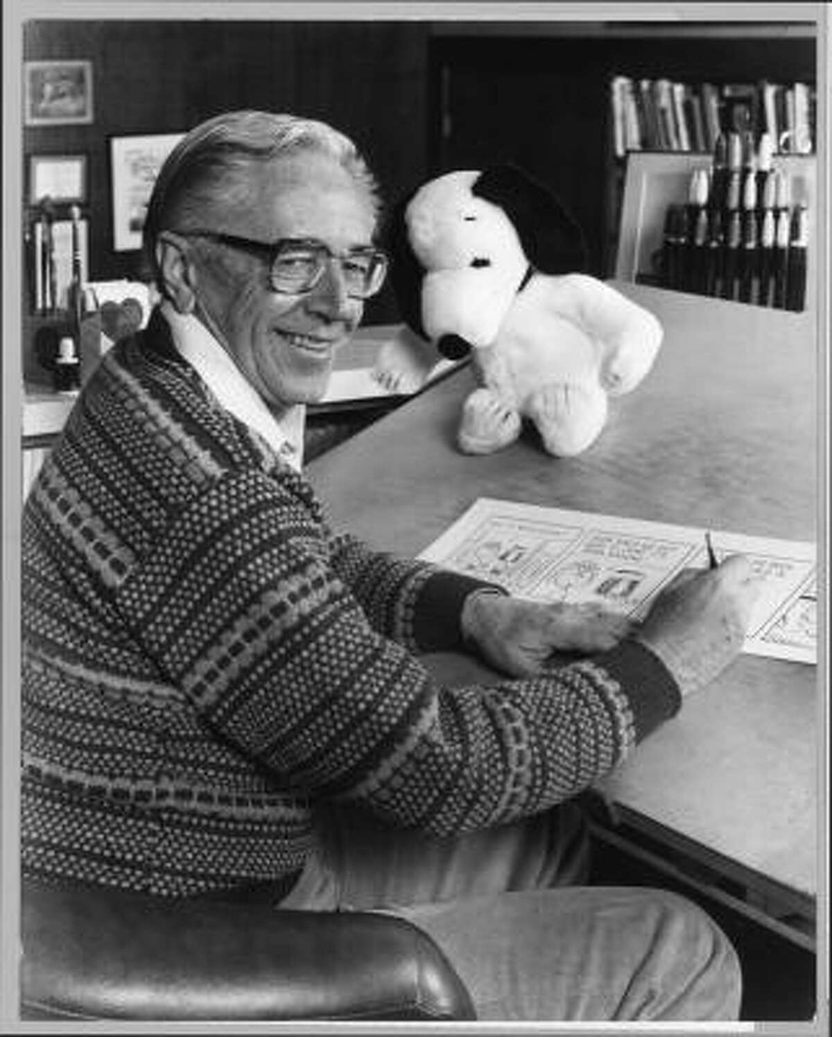 Charles Schulz at work in 1987 with a "Peanuts" strip and a plush Snoopy.