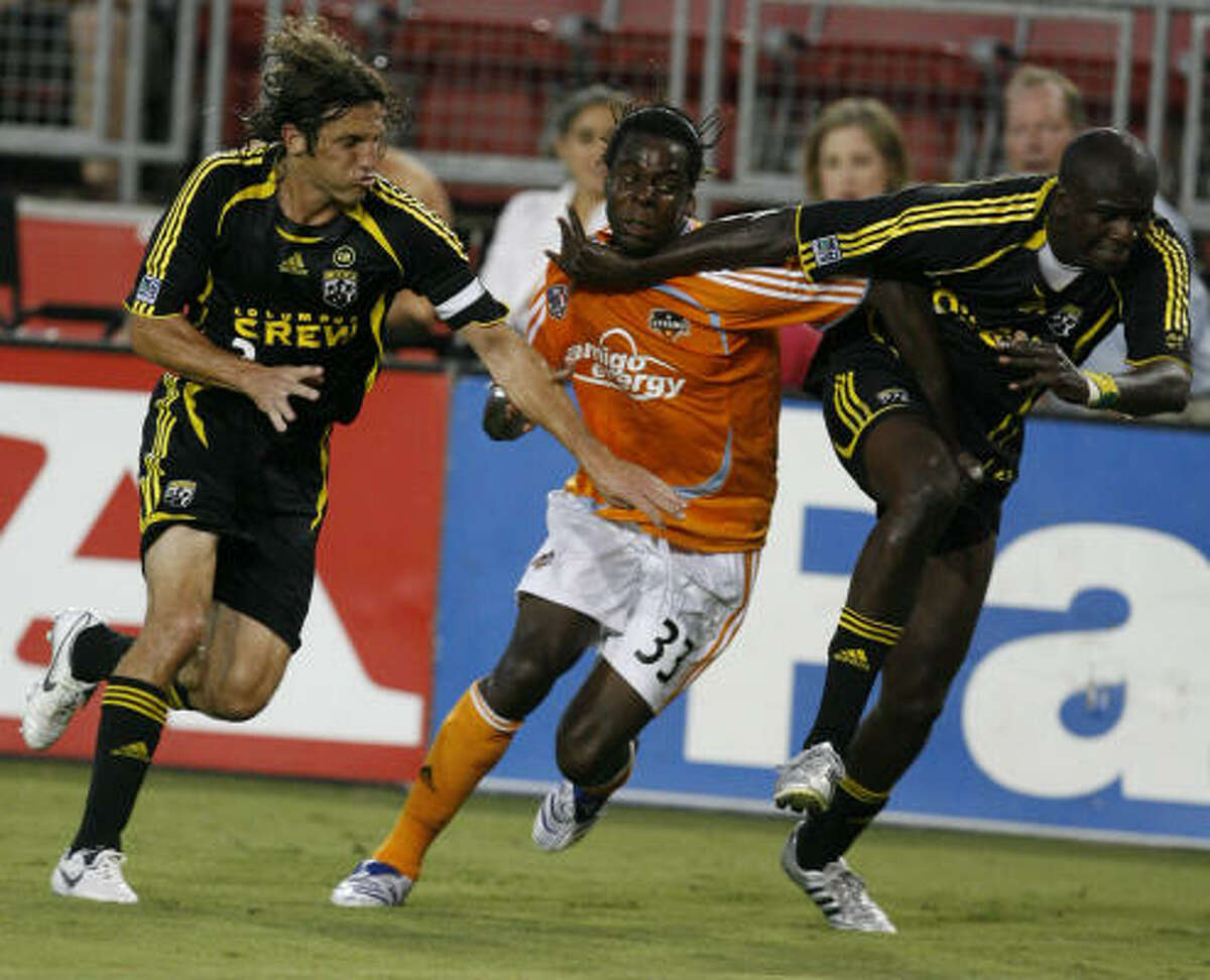 Joseph Ngwenya, center, is blocked by the Columbus Crew's Frankie Hejduk, left, and Ezra Hendrickson from chasing the play. The Dynamo extended their lead in the Western Conference to two points with a 1-1 tie.