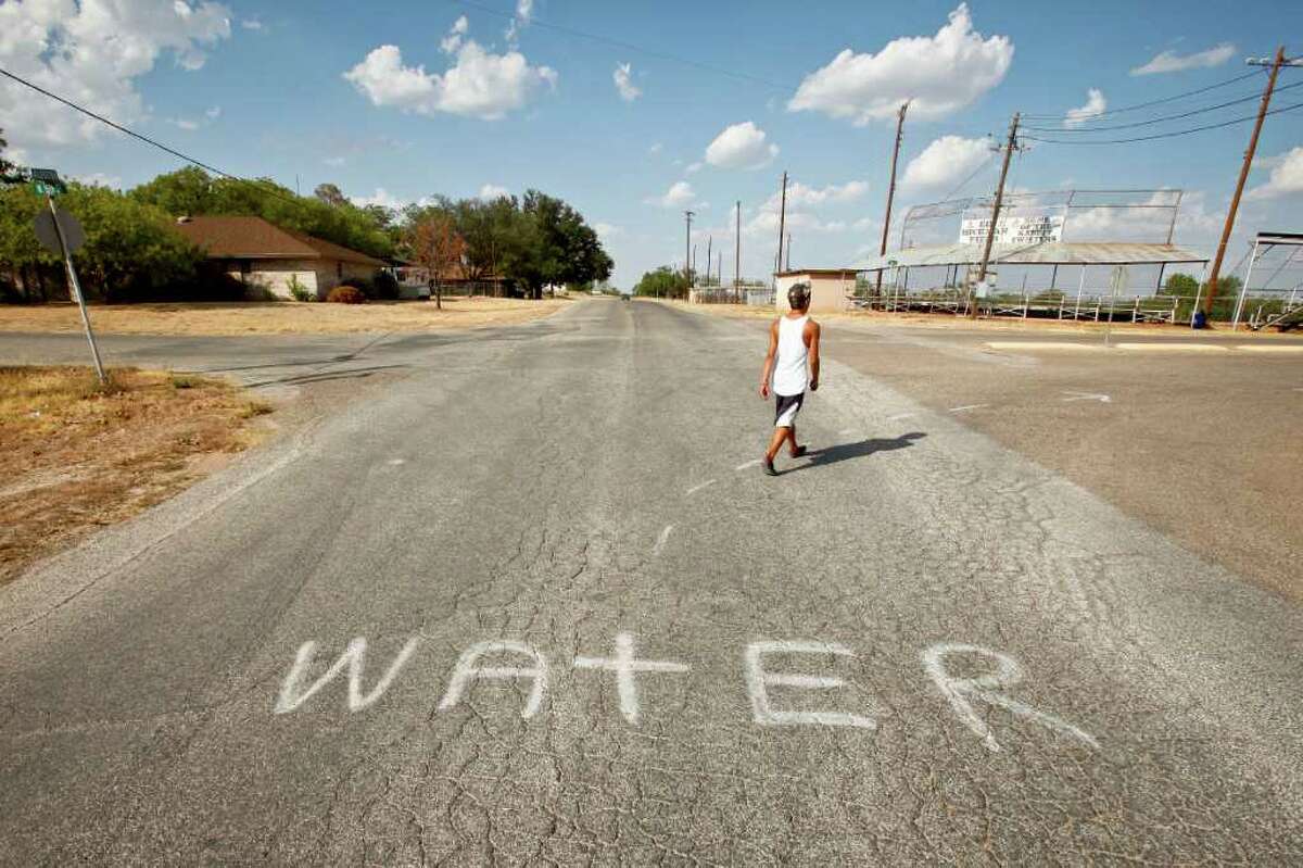 Jesus Landeros, 14, walks to the city pool and past a spray painted sign directing firefighters to a water source to fill their tankers while fighting the recent Wildcat Fire that threatened the town and burnt 160,000 acres, Wednesday, Aug. 10, 2011, in Robert Lee. The city's pool was recently used by a firefighting helicopter when it scooped several hundred gallons to be dropped on a nearby wildfire that threatened the town and burnt 160,000 acres. The city of Robert Lee is experiencing an unprecedented drought receiving around 3 inches of rain in the past year. The city's drinking water is nearly dried up coming from the local Lake E.V. Spence which is at .7% capacity. Families have been forced to conserve water cutting back from 20,000 gallons per family per month to 3,000 to 4,000 gallons. If the city continues to receive no significant rain fall, the city will run out of water by early 2012. ( Michael Paulsen / Houston Chronicle )