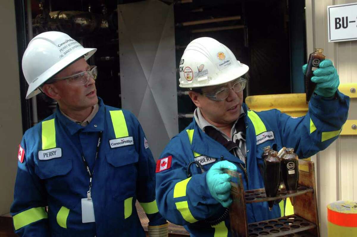 Robert Lee, a lab technician at ConocoPhillips' Surmont oil sands project in Alberta, examines a vial of water and oil sediment. Looking on is Perry Berkenpas, vice president of oil sands operations for ConocoPhillips Canada.