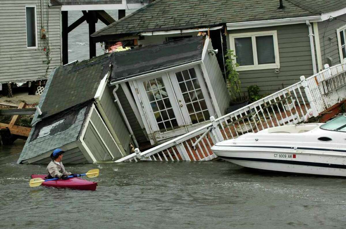 A kayaker pauses to look at a Fairfield Beach Road home that fell into Pine Creek in Fairfield, Conn. as treacherous weather caused by Hurricane Irene came through the area on Sunday Aug. 28, 2011.