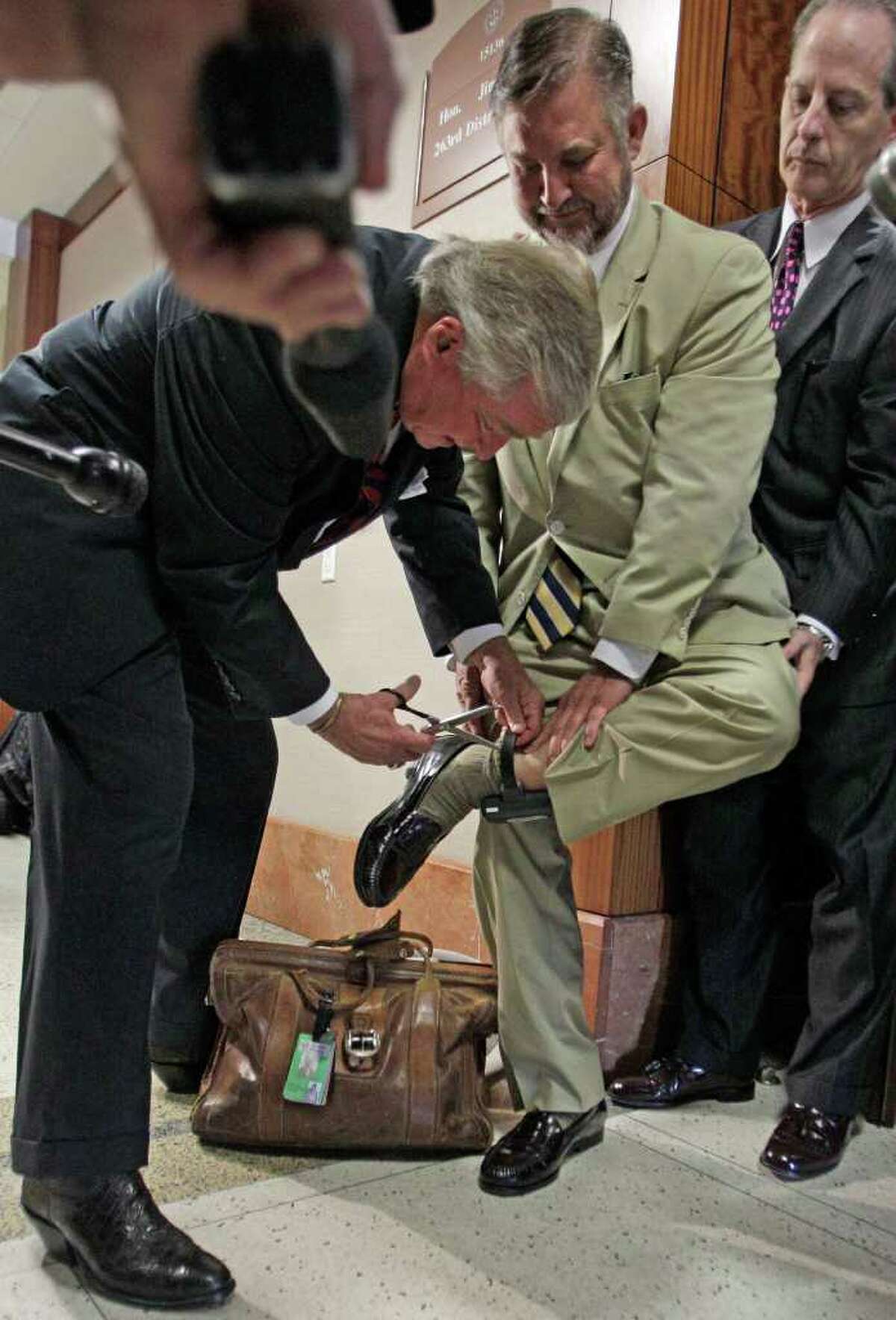 MELISSA PHILLIP : CHRONICLE CLEARED: Defense attorney Dick DeGuerin cuts the monitoring device from the ankle of his client, Michael Brown, after the verdict. Defense attorney Brian Wice steadies Brown.