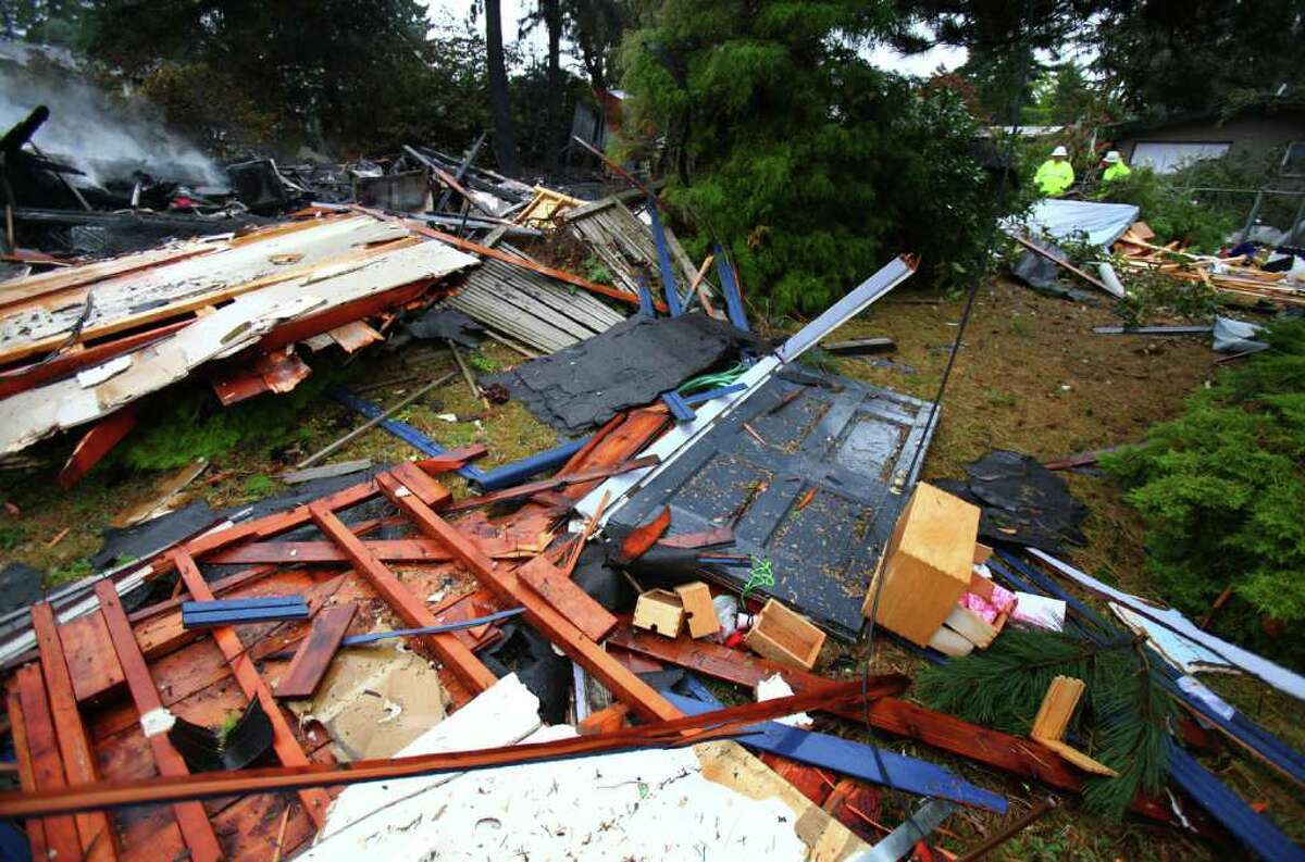 A Puget Sound Energy crew, upper right, investigates after a natural gas explosion destroyed a home, sent debris across a neighborhood and severely injured a man and a woman, on Monday in North Seattle. The explosion shattered windows for blocks. The shock wave was felt for miles.
