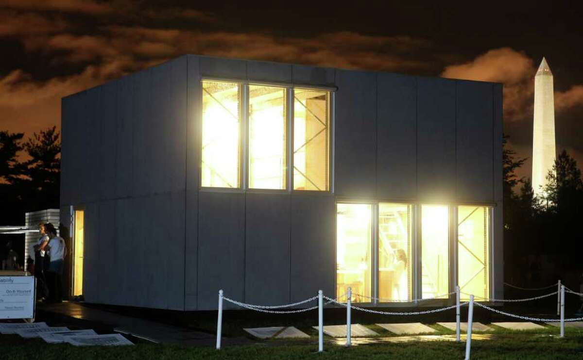 The exterior of E-Cube, by Team Belgium, is pictured at night on Sept. 23, 2011 at the U.S. Department of Energy Solar Decathlon 2011 in Washington, D.C. The building is envisioned as an affordable kit that can be assembled in days, thanks to such approaches as: A façade made of fiber-cement boards with the same dimensions as the triple-glazed window elements; An interior stripped of most conventional finishes, saving on materials and easing construction; A standard pallet rack system that creates the main structure using a bolt-less assembly process; A plug-and-play electrical wiring system that is integrated into the structure for easy installation; A floor plan that can be expanded by adding more floor panels on the existing beams.