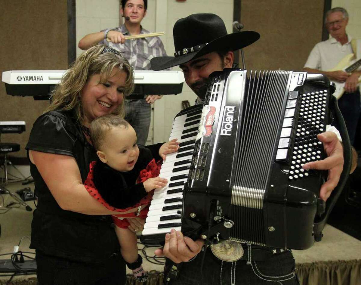 Kristina Rybak, eight months, tries her hand at playing the accordion with her dad Chris Rybak (right, foreground) as her mother Edita Rybak (left) holds her at the Knights of Columbus Hall on Rigsby Road during the Bexar County Czech Society's annual festival. Kristina Rybak met her husband Chris at the festival 14 years ago.