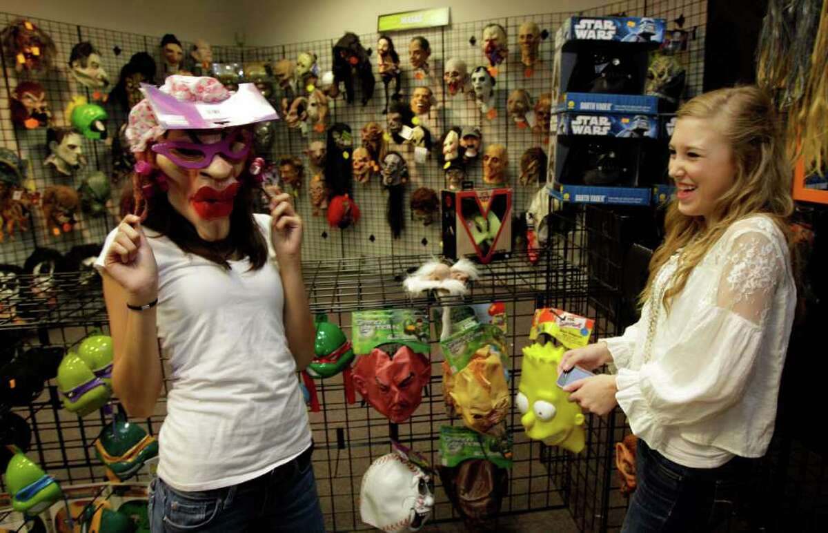 SCARING UP SALES: Nadia Khan, left, and Maddie Marlow, both 16 and from Sugar Land, have fun trying on masks at Halloween Express.