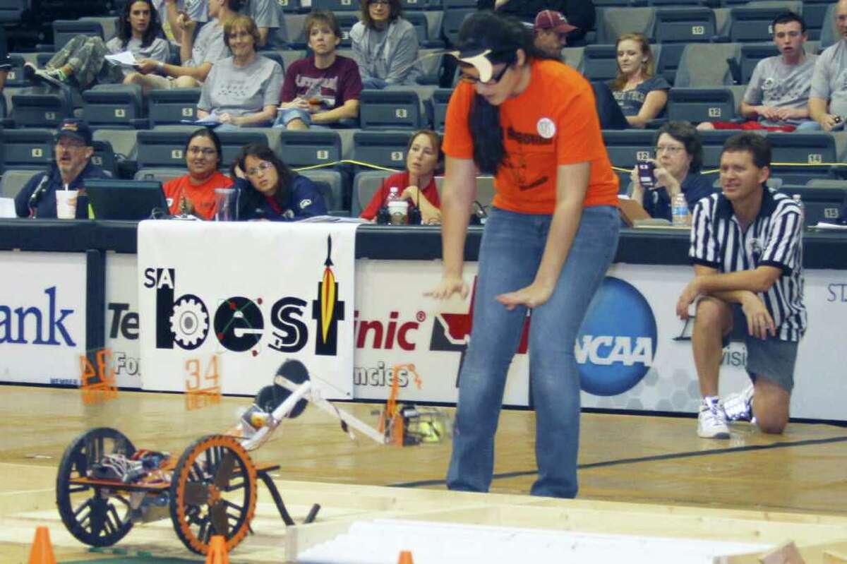 FORREST M. MIMS III COMPETING: A spotter helps a robot driver drop a "bug" into a containment area under the watchful eyes of judges and a referee at the 2011 San Antonio BEST Robotics Competition.
