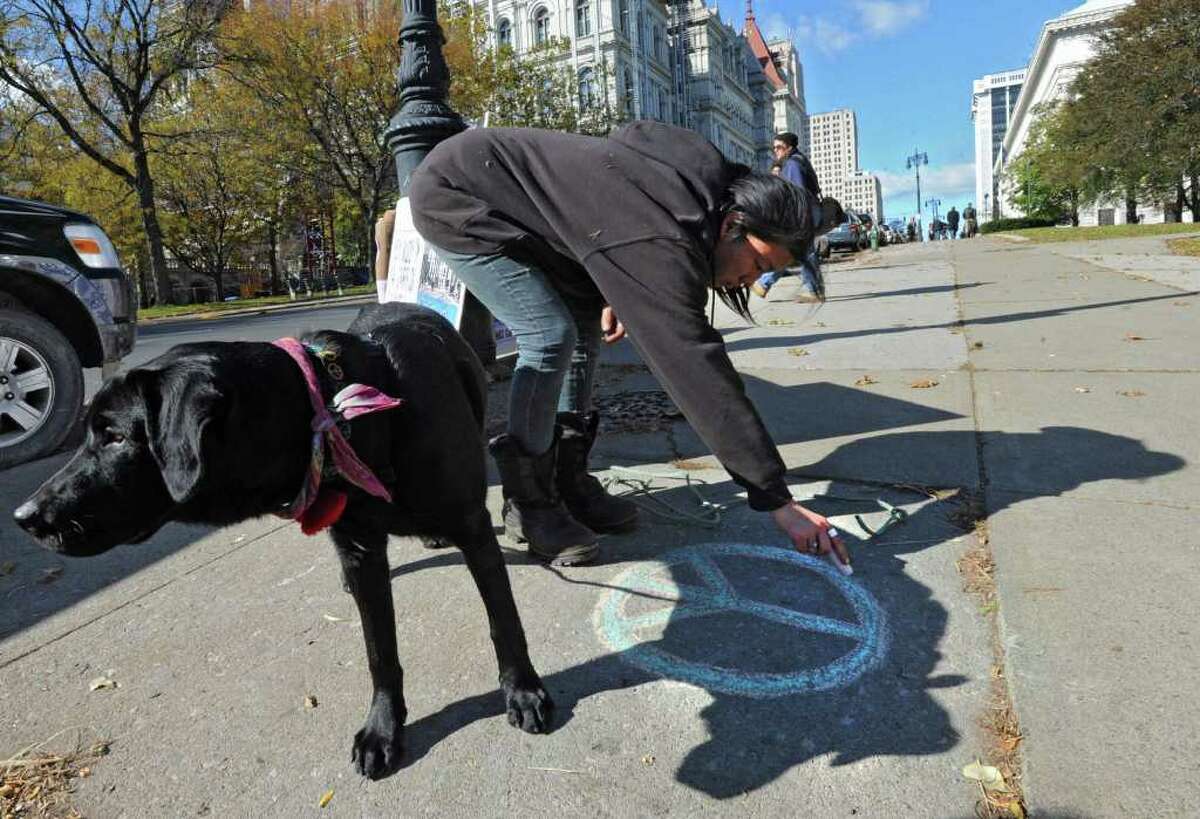 Occupy Albany marcher Soojee Eckardt-Rigberg of Delmar holds her dog Obi as she draws a peace symbol on the sidewalk with chaulk before marching down State St. to Bank of America in Albany, N.Y. Friday, Nov. 4, 2011. The marchers were urging people to close their bank accounts at Bank of America and open an account with a credit union such as SEFCU. (Lori Van Buren / Times Union)