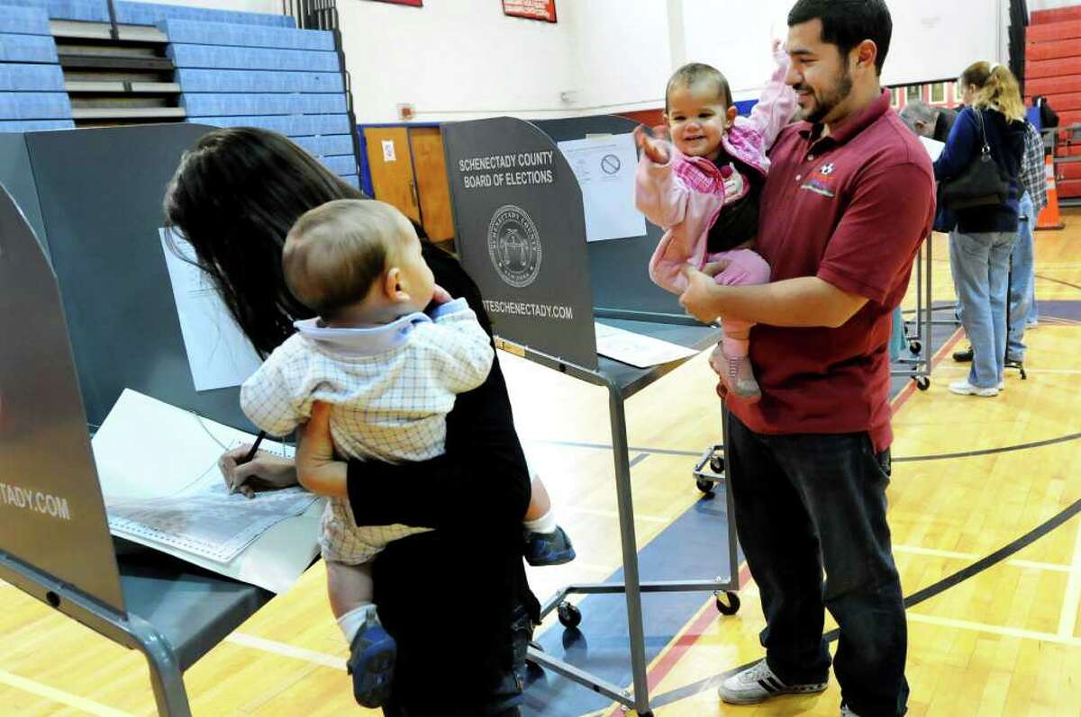 Peter Testa, right, holds daughter Sabine, 19 months, while his wife, Mary Ellen, votes on Election Day on Tuesday, Nov. 8, 2011, at Schenectady High in Schenectady, N.Y. Sabine waves at her brother Pellegrino, 6 months. The couple had to take turns between watching Sabine and voting. (Cindy Schultz / Times Union)