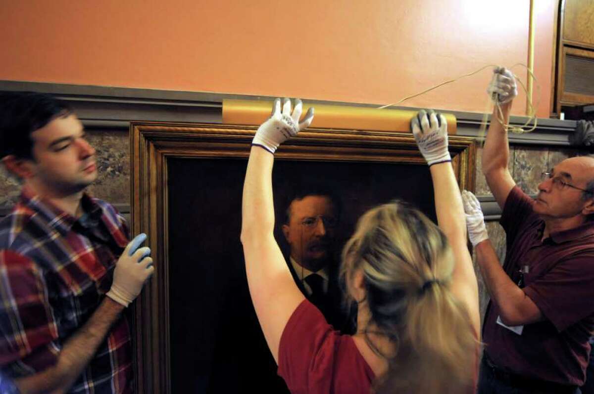 State Museum specialists, from left, Owen Sherwood, Koren Lazarou-Egnaczyk and Michael Carlito remove the light from the frame of a painting of Theodore Roosevelt as workers from the museum and state Office of General Services removed the paintings of past governors from the walls in the Hall of Governors on the second floor of the Capitol on Tuesday, Nov. 15, 2011. The paintings will be cleaned and then new frames and better lighting will be installed for the paintings when they are returned to the hallway. (Paul Buckowski / Times Union)