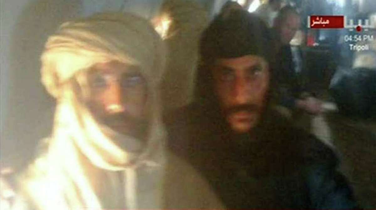 In this image from Libyan Television, Seif al-Islam Gadhafi, left, is guarded by a Libyan fighter as he is transported to Zintan, Libya, by a transport aircraft following his capture near the Niger border early Saturday Nov 19 2011. Moammar Gadhafi's son, the only wanted member of the ousted ruling family to remain at large _ was captured as he traveled with aides in a convoy in Libya's southern desert.