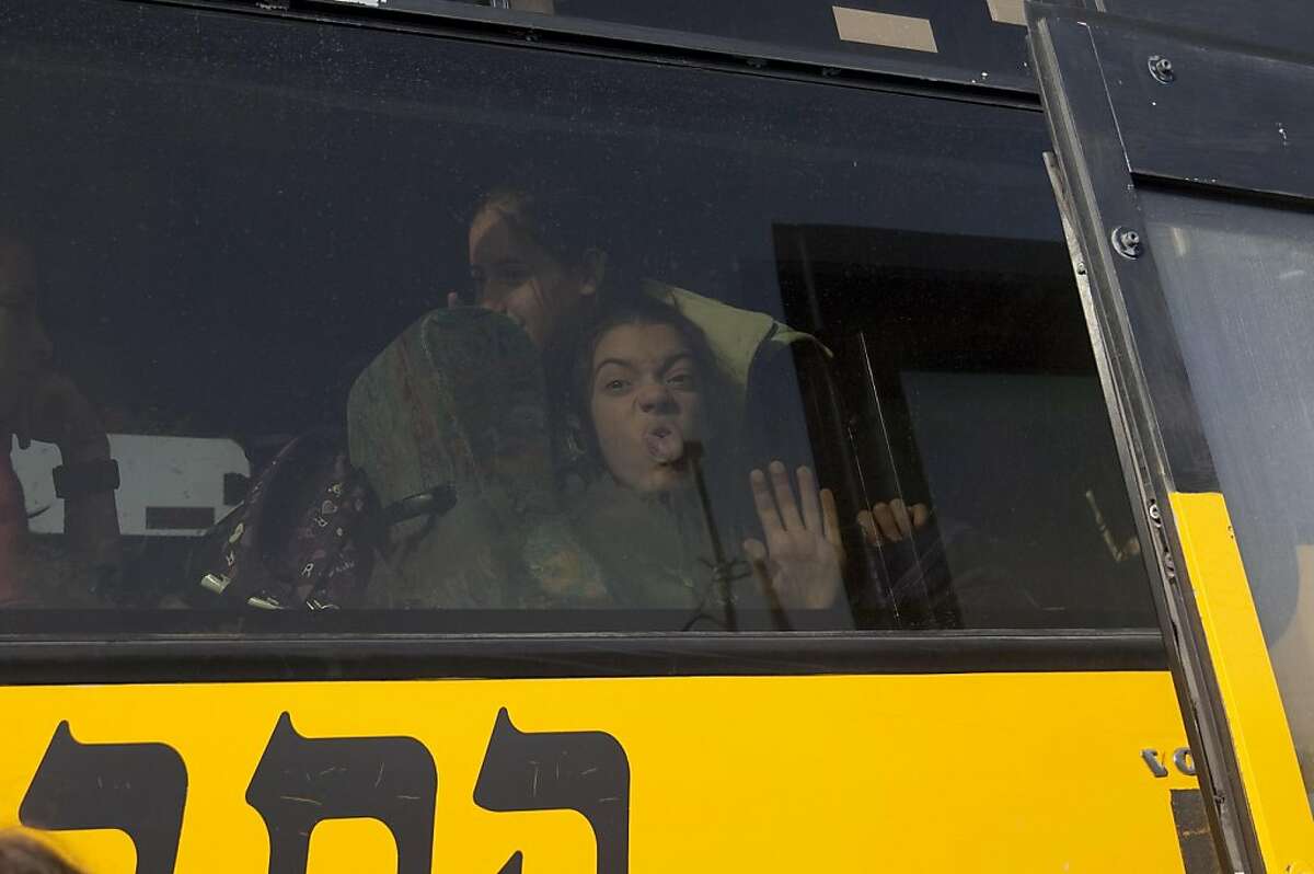 A young Israeli settler grimaces from inside a bus as media and Palestinian activists gather at a bus stop outside the West Bank Israeli settlement of Migron, near Ramallah, on November 15, 2011. Palestinian "Freedom Riders" reenacted US civil rights movement's boarding of segregated buses in the American south by riding Israeli settler buses to Jerusalem. Several Israeli transportation companies operate dozens of lines that run through the occupied West Bank and east Jerusalem, many of them subsidized by the state. While it is not officially forbidden for Palestinians to use Israeli public transportation in the West Bank, these lines are effectively segregated, since many of them pass through Jewish-only settlements, to which Palestinian entry is prohibited by a military decree. AFP PHOTO/AHMAD GHARABLI (Photo credit should read AHMAD GHARABLI/AFP/Getty Images)