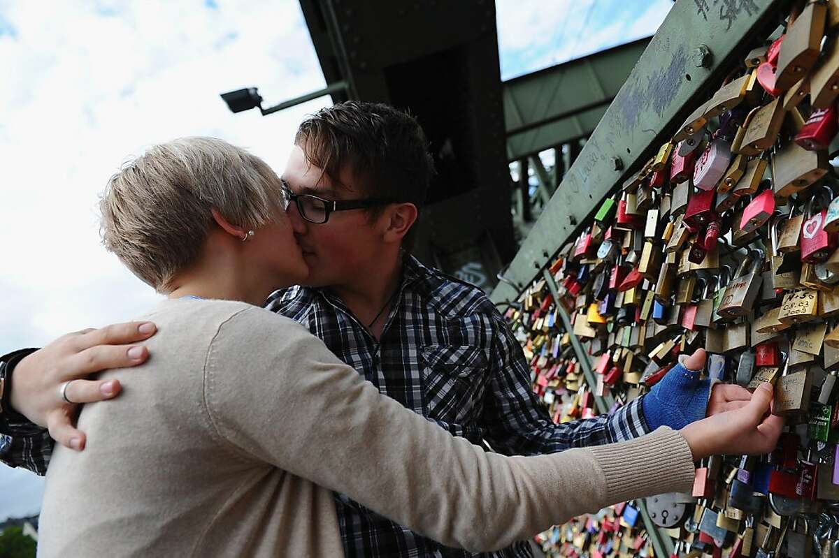 COLOGNE, GERMANY - SEPTEMBER 13: A young couple kisses next to their personal love lock locked on some time ago. Thousands of so-called "love locks," or "love padlocks," hang from a fence across the Hohenzollernbruecke bridge on September 13, 2011 in Cologne, Germany. Love locks are a growing phenomenon in cities across Europe and are meant by the couples who leave them behind as a symbol of their powerful and undying love for one another. (Photo by Dennis Grombkowski/Getty Images)
