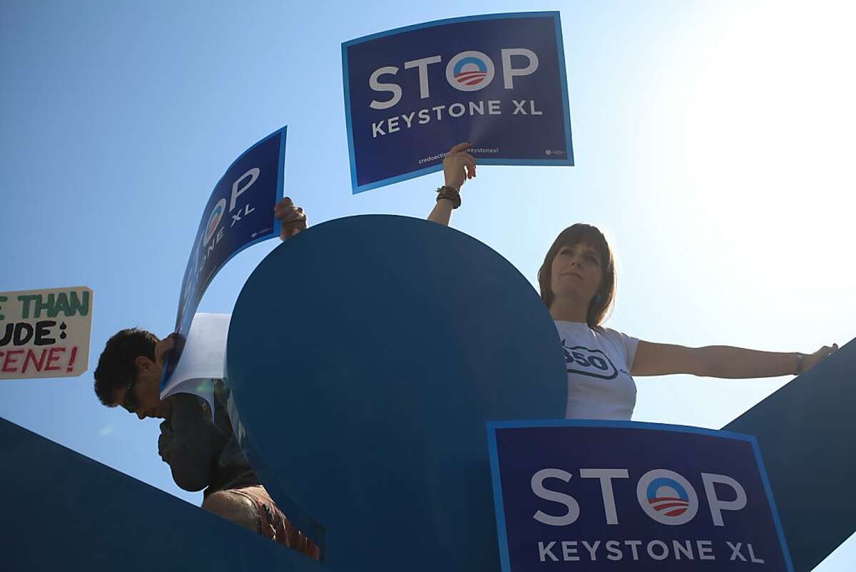 Josh Newman and Amanda Ravenhill, both of San Francisco stand atop a Keith Harring sculpture holding signs protesting the proposed Keystone XL pipeline project outside the W Hotel, where the president attended a fundraiser in San Francisco, Calif. on Tuesday, October 25, 2011.
