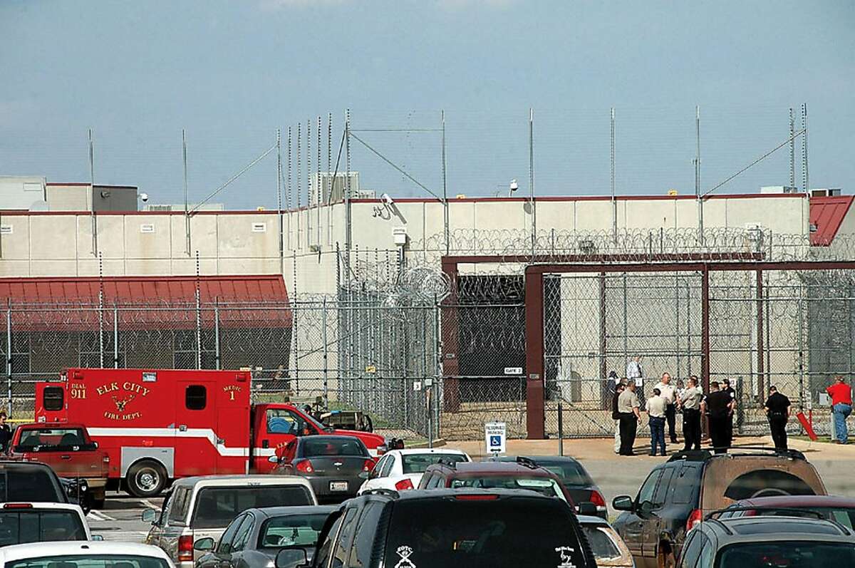 Emergency vehicles an authorities standby at the entrance to the North Fork Corrections Facility in Sayre, Okla. Tuesday, Oct. 11, 2011. Inmates were confined to their cells and their movements restricted after widespread fighting at an Oklahoma prison between black and Hispanic California inmates sent at least 46 inmates to the infirmary or hospitals before police and prison guards were able to restore order, authorities said Tuesday. (AP Photo/ Elk City Daily News, Jodi Davis)