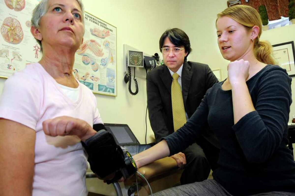 Occupational therapist Amy Boos assists an aneurysm patient, Kathy Riordan, with the mPower 1000 in neurologist Dr. Frederick Nahm's Greenwich office as Nahm looks on. Manufactured by the neurorobotics company Myomo, the robotic device harnesses patients' own limited muscle movement to help them use their arms.