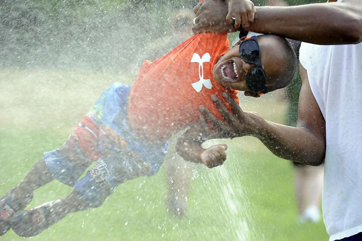 Terrence Smith, 6, gets a lift from his dad, Eric Smith, in the sprinklers in the South Meadow at Snug Harbor Cultural Center and Botanical Garden, on Friday, July 22, 2011, in New York. The center hosted "Sprinkler Fest" to help people cool off as the temperatures in and around New York City exceeded 100 degrees. (AP Photo/The Advance, Bill Lyons) NYC LOCALS OUT; NO SALES; ONLINE OUT
