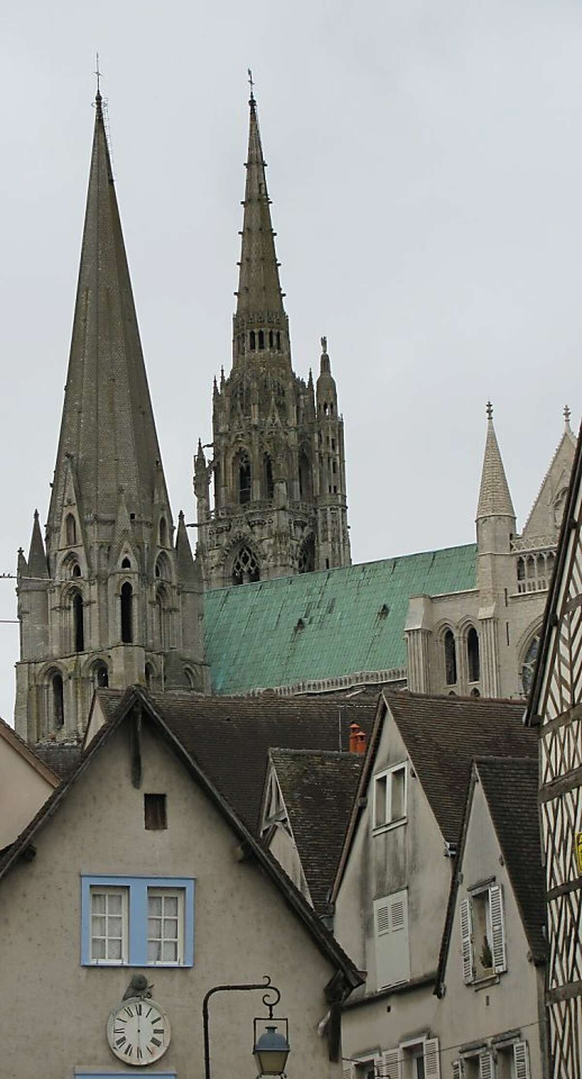 The spires of Chartres Cathedral seen from the banks of the Eure River, with a half-timbered building in the foreground.