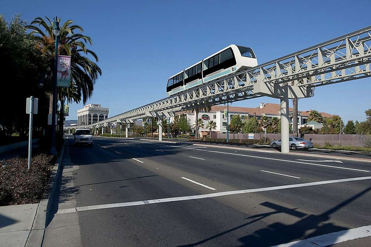 An artist's rendering shows the Oakland Airport Connector Automated People Mover (APM) System in the median of Hegenberger Road between I-880 and Doolittle Drive. The vehicle system is to be manufactured and operated by Doppelmayr Cable Car and is shown on a steel guideway supported by concrete columns.