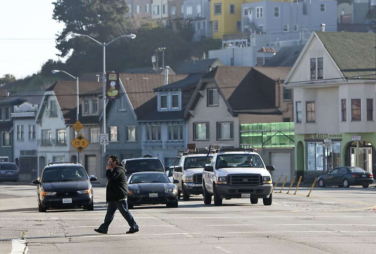 A pedestrian crosses Cesar Chavez Street as motorists wait at a stoplight on the street in San Francisco, Calif., on Thursday, January 6, 2011. The city has unveiled a plan to remake the street with fewer traffic lanes, a new pedestrian plaza and new medium plantings.