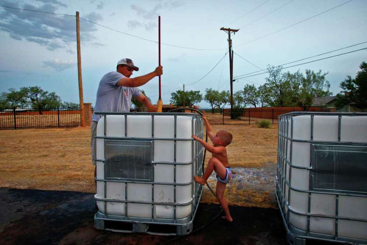 Brennen Hood, 3, tries to help his father, Aaron Hood, school superintendent and athletic director for Robert Lee High School, as he cleans out large chemical containers which will be used as water hauling tanks, at his home. Each tank holds nearly 250 gallons of water and residents of Robert Lee are forced to drive to neighboring cities to find water to be used for watering lawns and trees.