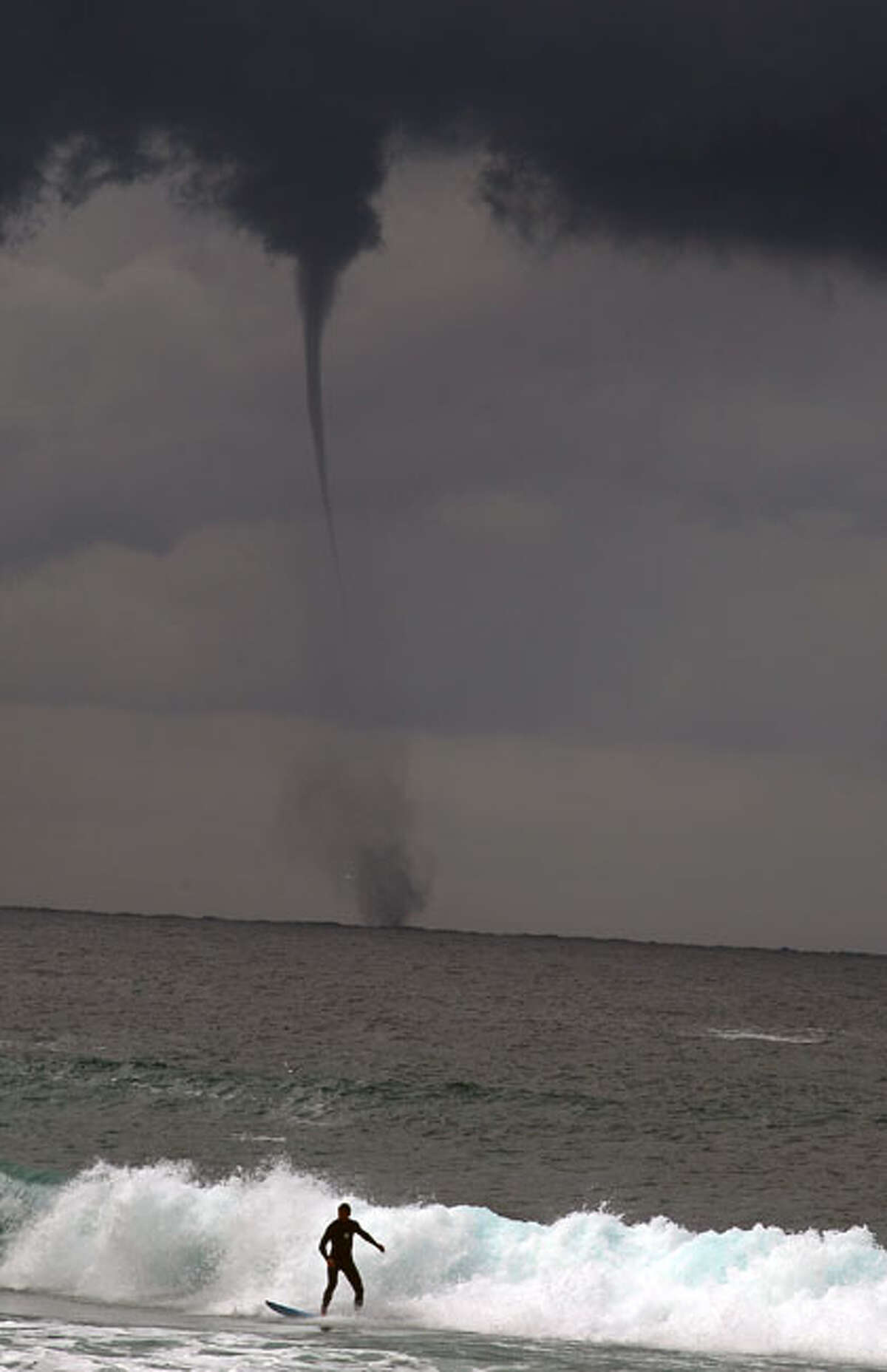 A water spout (tornado) hits the sea behind a surfer on Sydney's Bondi Beach on May 17, 2010. A rare sight in Australia, the water spout lasted around five minutes and expired before landfall.