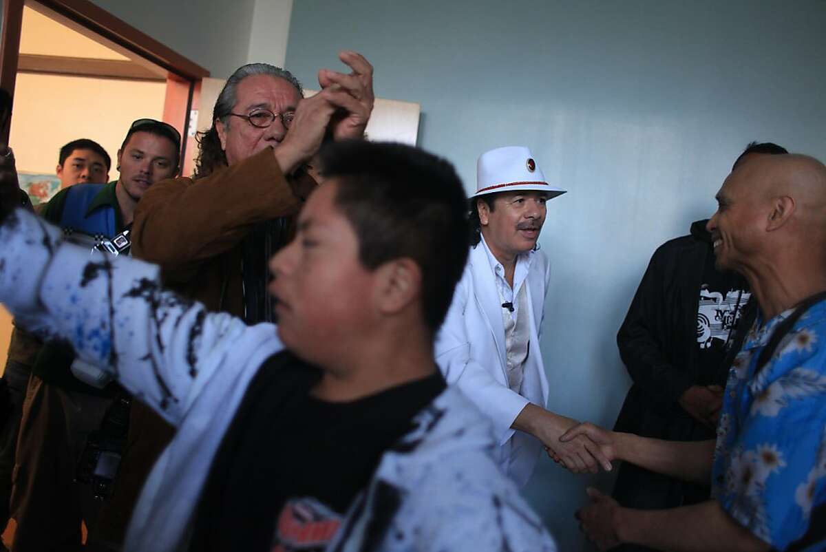Carlos Santana (third from right) greets special education dance drum circle teacher Benito Santiago (right) while touring his alma mater Mission High school with his wife Cindy Blackman Santana (not shown), Edward James Olmos (third from left), and and Peter Bratt (partially seen second from right) in San Francisco, Calif. on Monday, October 24, 2011.